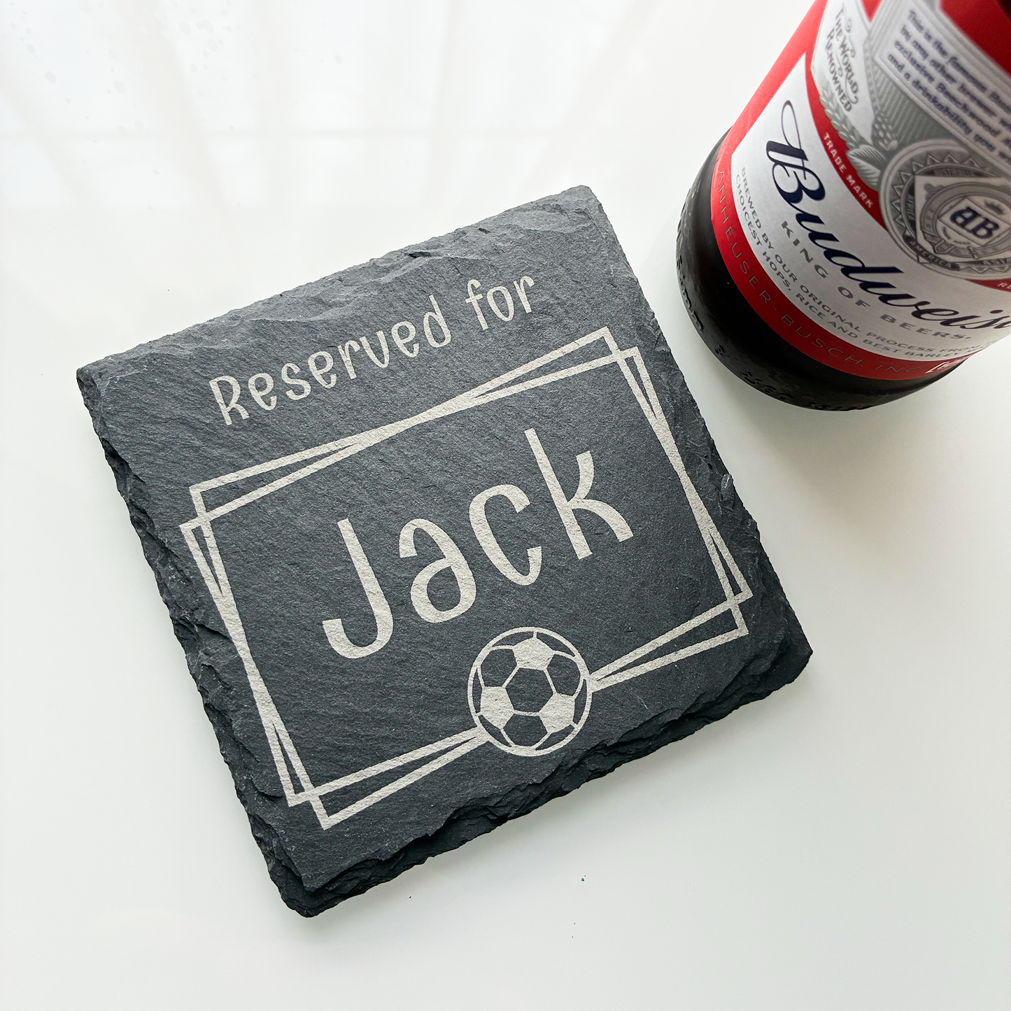 Square slate coaster with 'Reserved for Jack' engraving next to a Budweiser bottle on a white surface