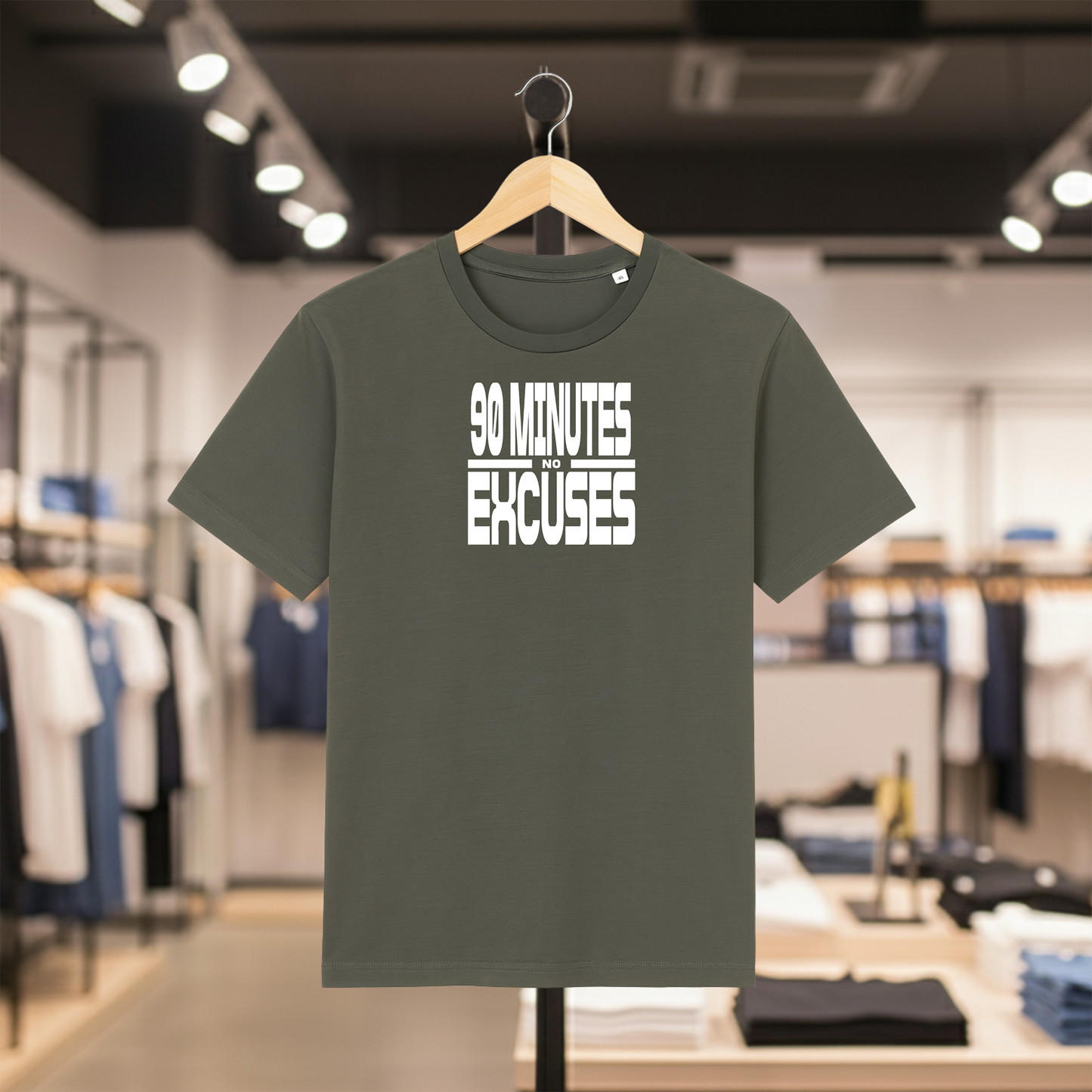 Khaki t-shirt with '90 Minutes No Excuses' text on a hanger in a clothing store.