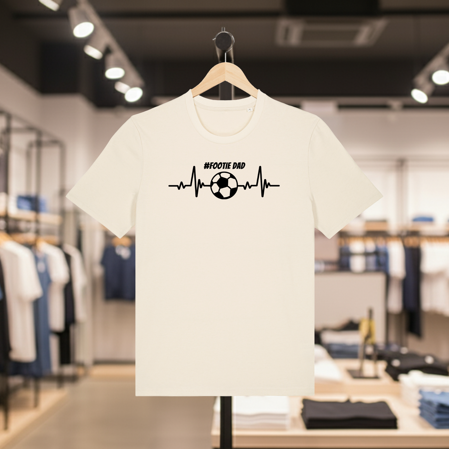 Natural t-shirt with '#FOOTIE DAD' design on a hanger in a store.