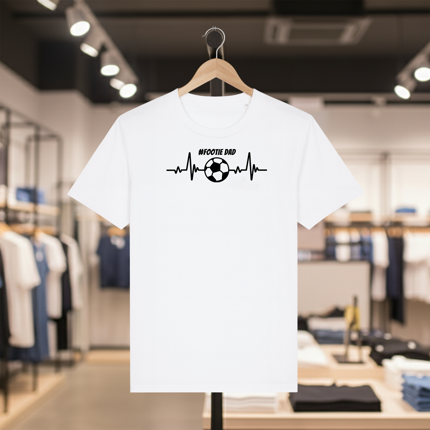 White t-shirt with '#FOOTIE DAD' design on a hanger in a store.