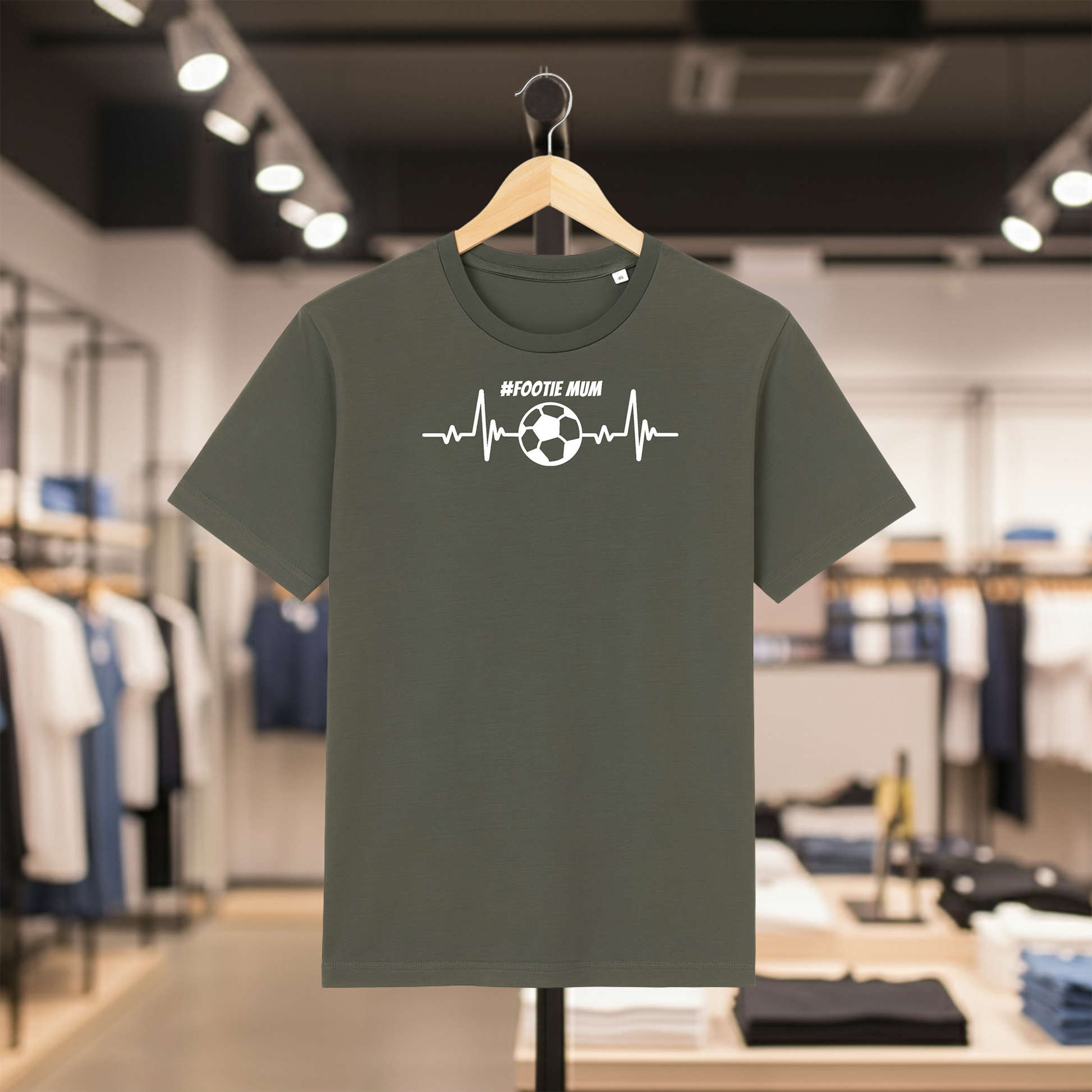 Khaki t-shirt with '#FOOTIE MUM' design on a hanger in a store.