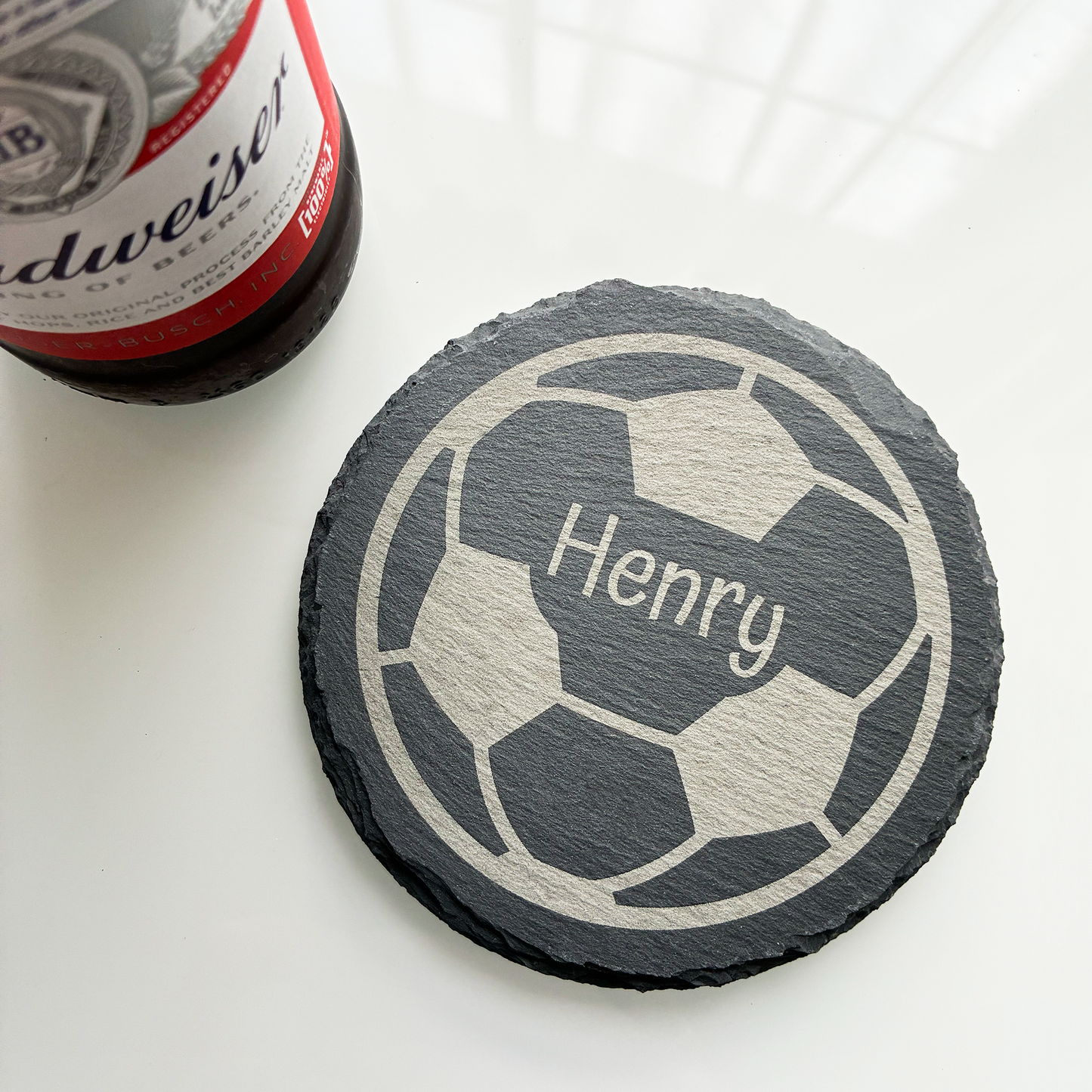 Slate coaster with soccer ball design and 'Henry' engraving next to a Budweiser bottle.