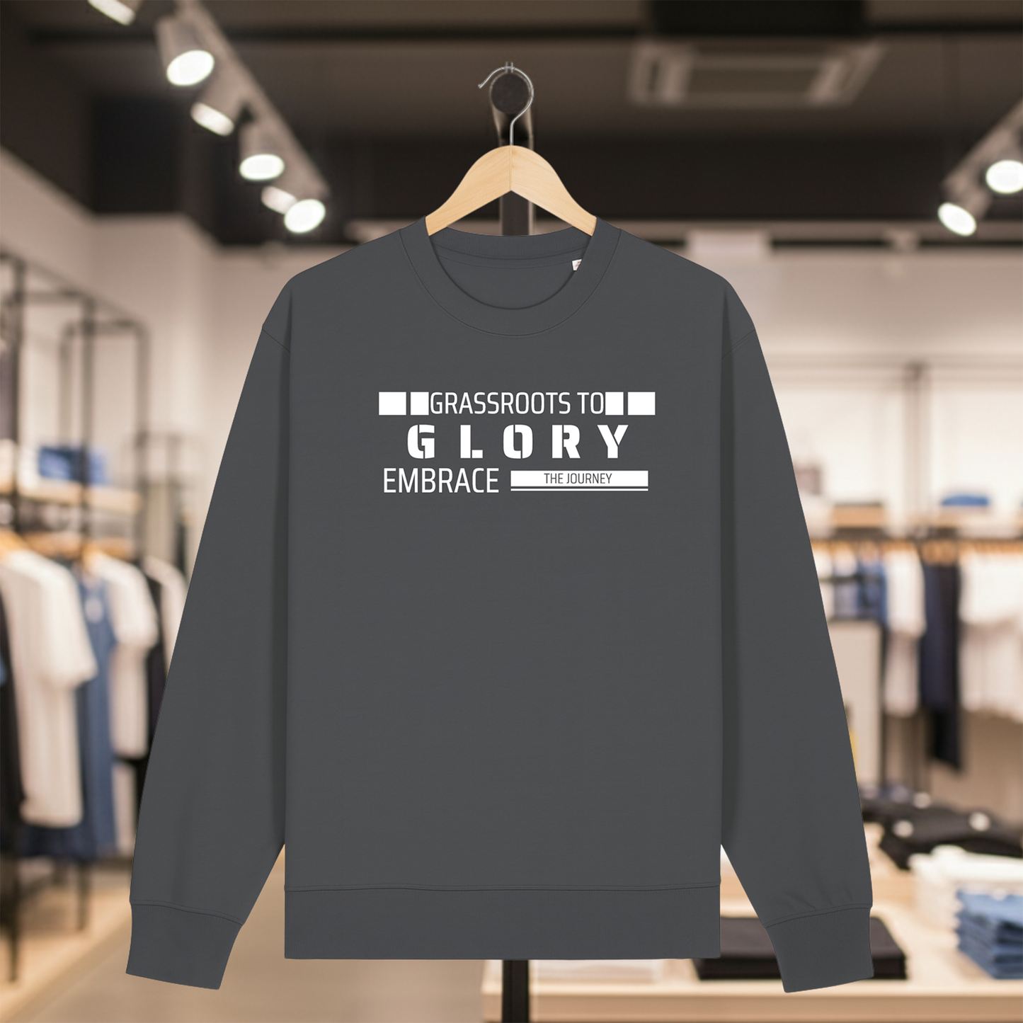 Grey sweatshirt with text GRASSROOTS TO GLORY on a hanger in a store setting
