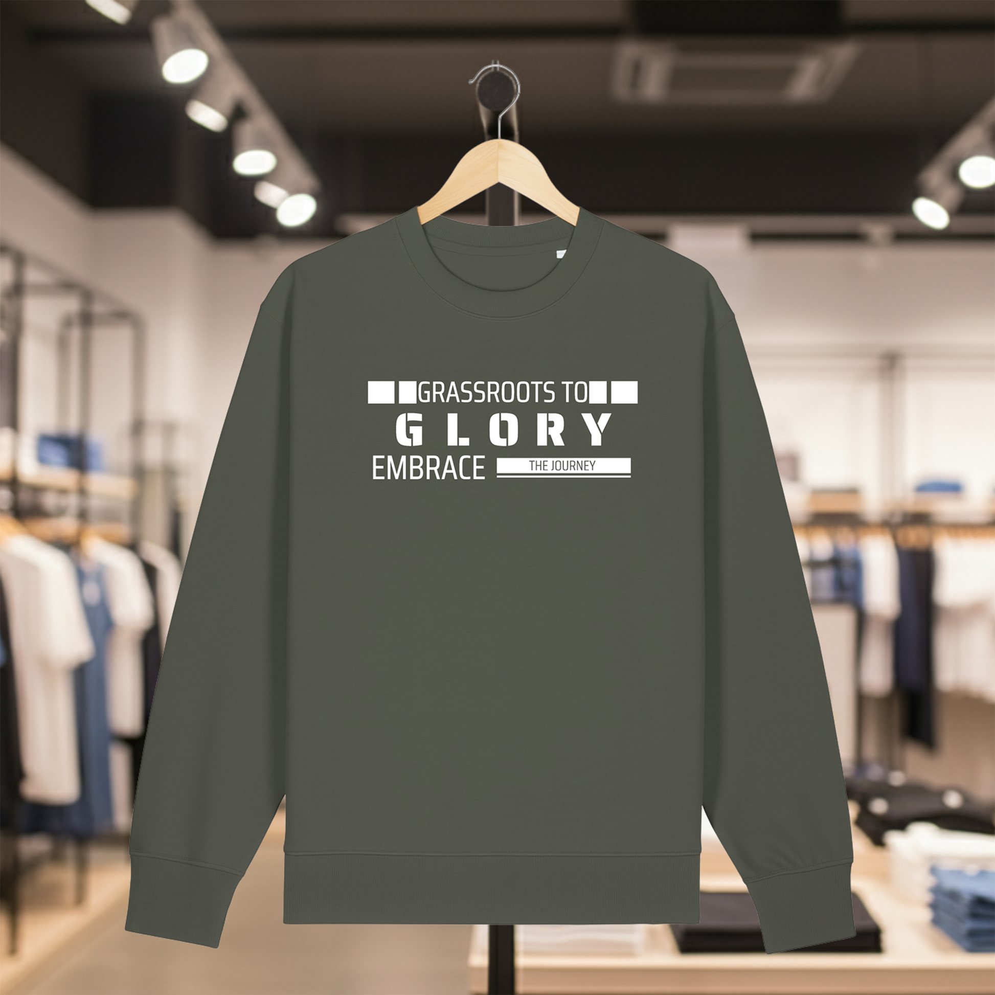 Khaki sweatshirt with text GRASSROOTS TO GLORY on a hanger in a store setting