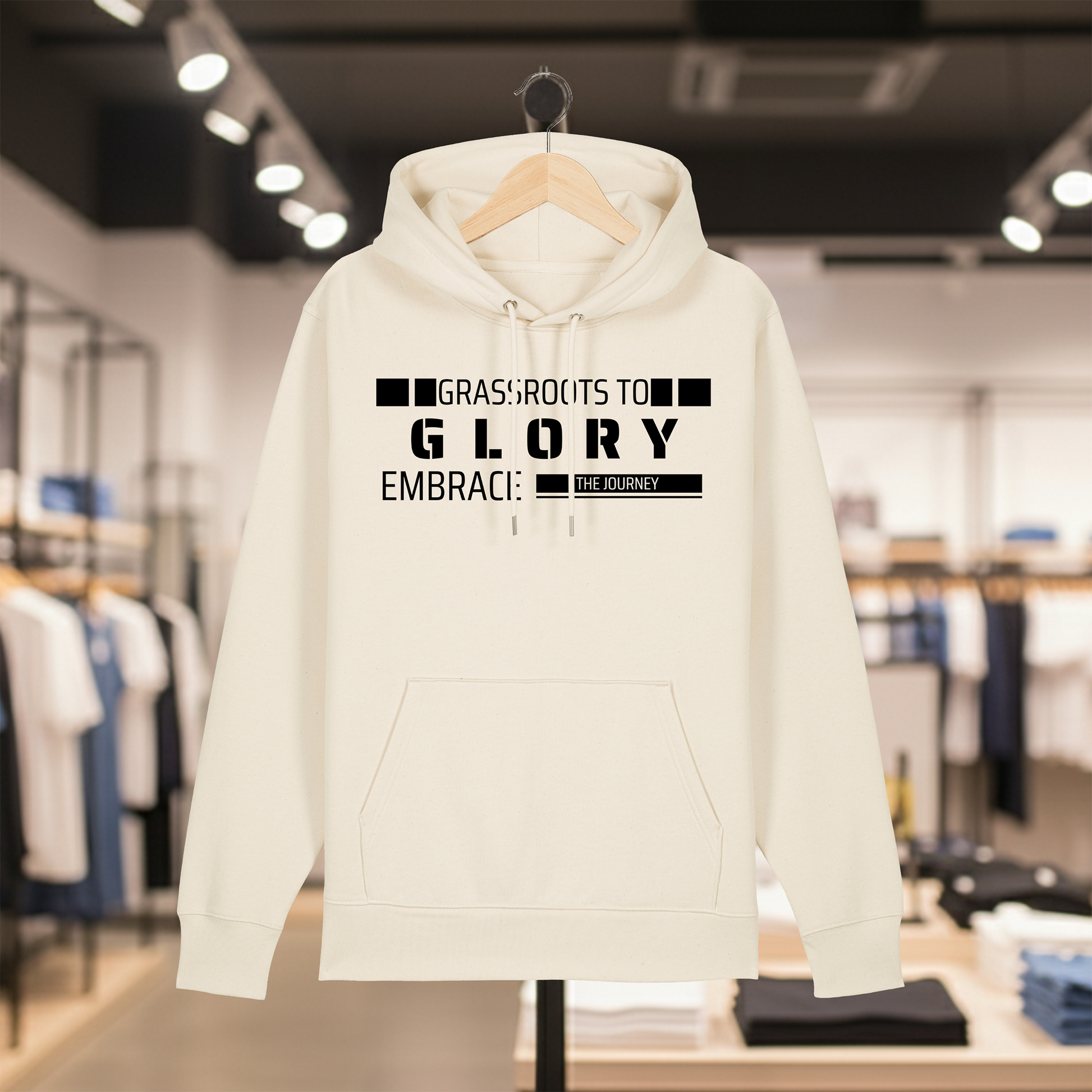 Natural hoodie with text GRASSROOTS TO GLORY on a hanger in a store setting