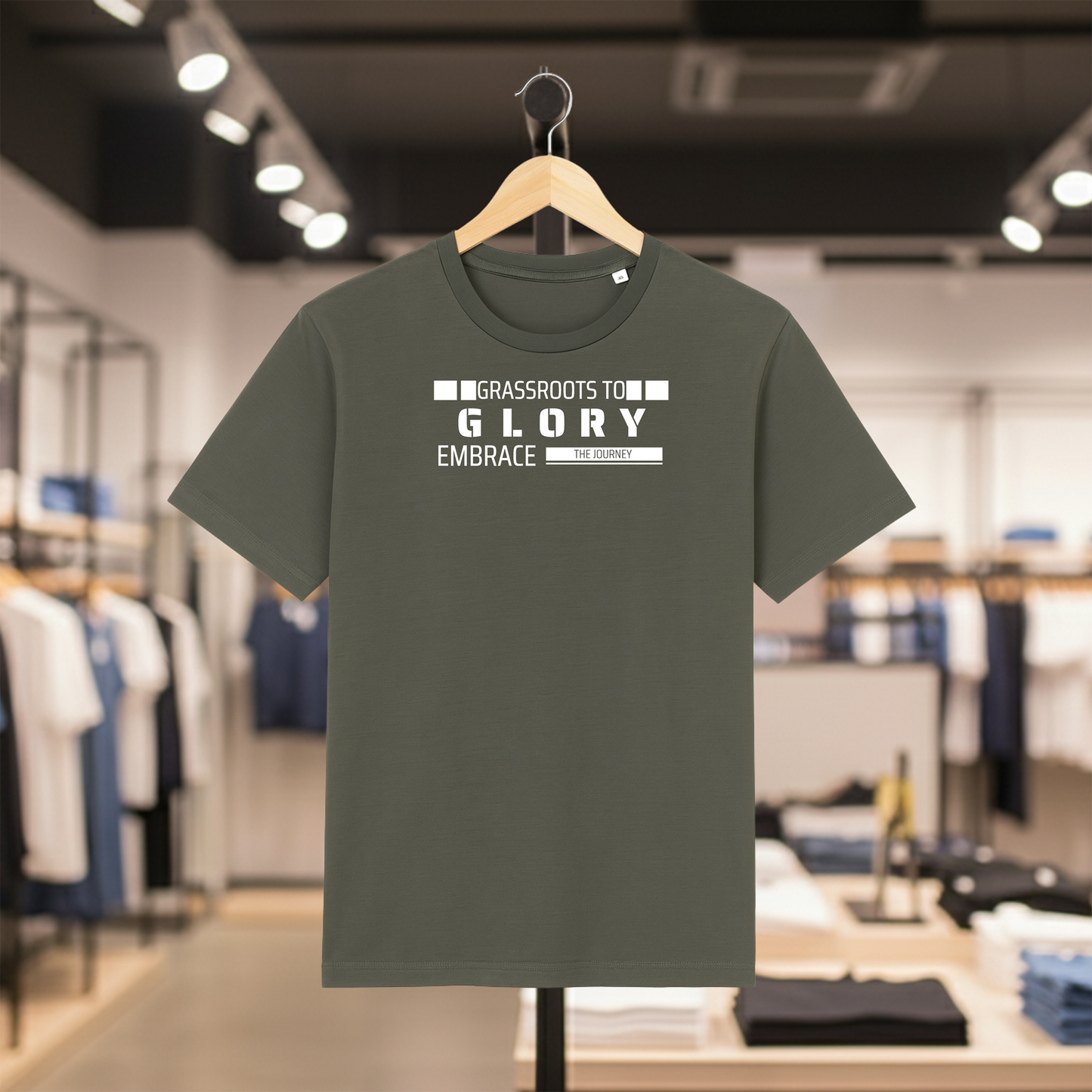 Khaki t-shirt with Grassroots to Glory design on a hanger in a store setting