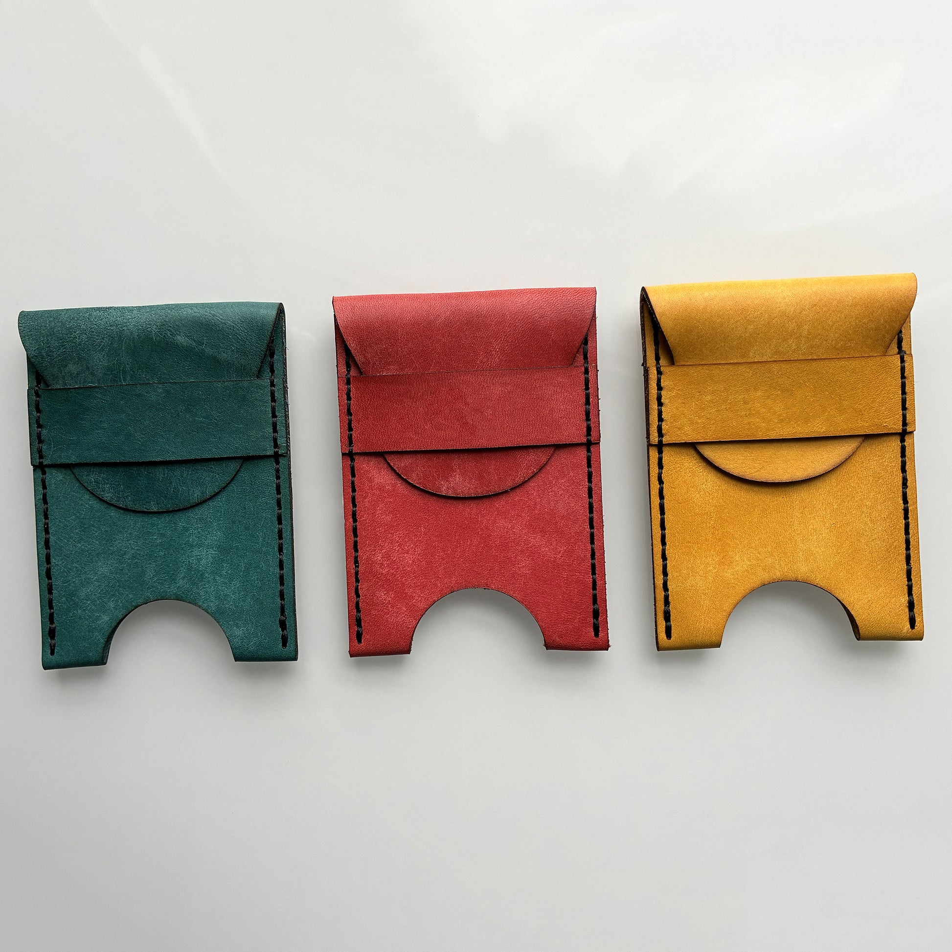 Three colourful leather card holders on a light grey background
