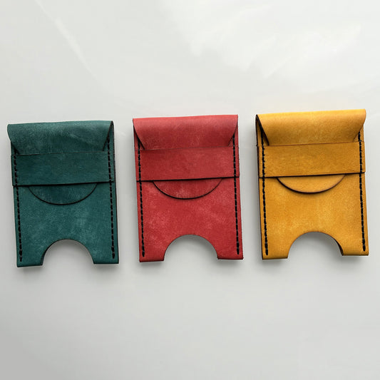 Three colourful leather card holders on a light grey background