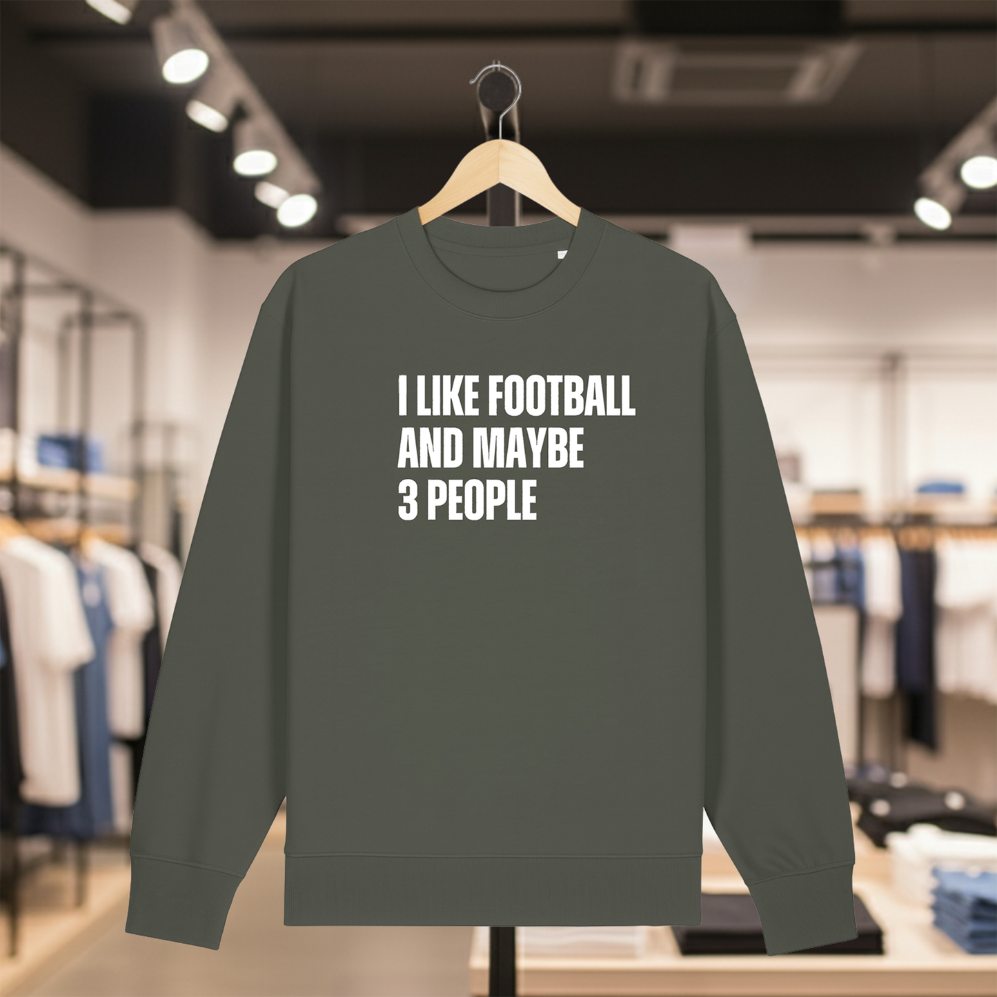 Khaki sweatshirt with text I LIKE FOOTBALL AND MAYBE 3 PEOPLE on a hanger in a store.