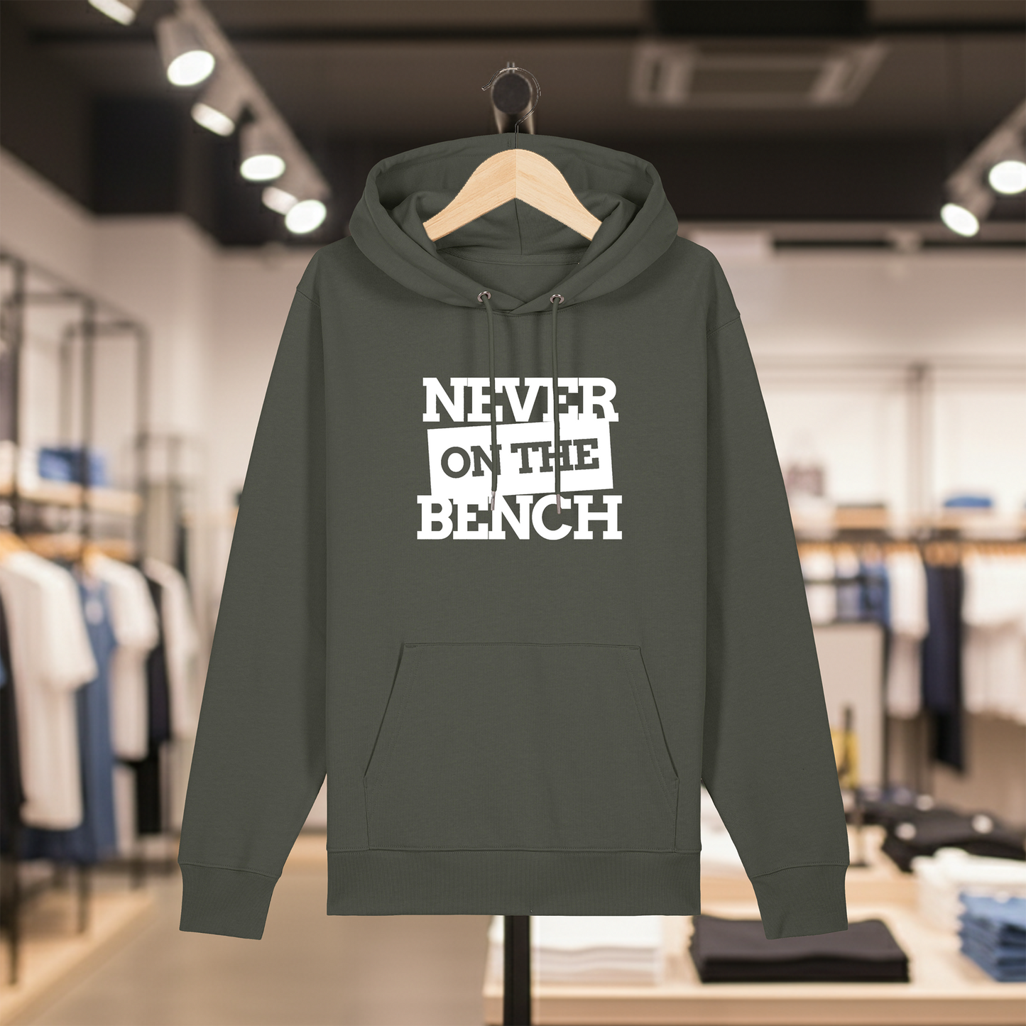 Khaki hoodie with text NEVER ON THE BENCH on a hanger in a store setting