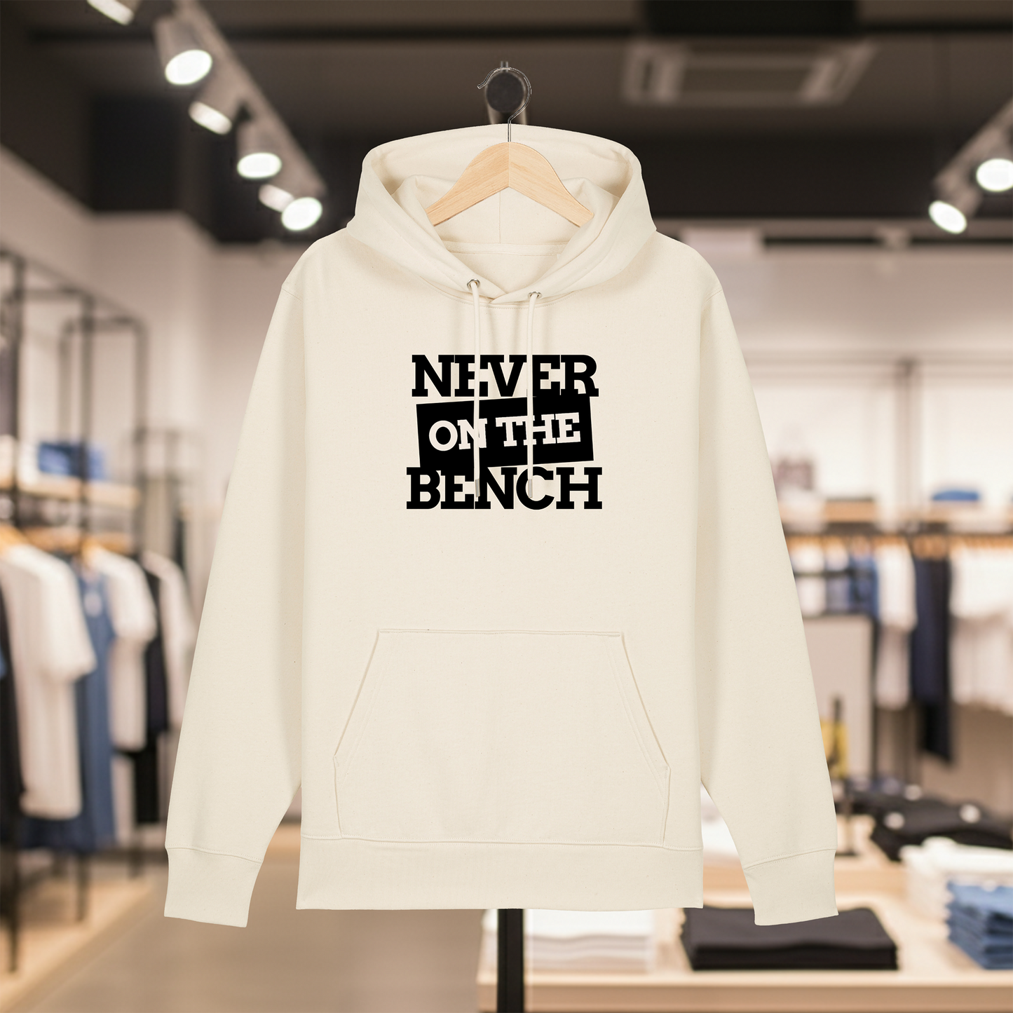 Natural hoodie with text NEVER ON THE BENCH on a hanger in a store setting