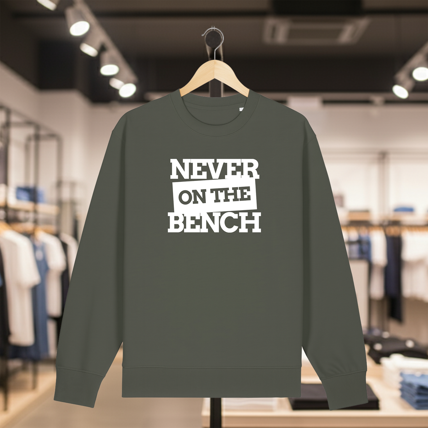 Khaki sweatshirt with NEVER ON THE BENCH text on a hanger in a store setting