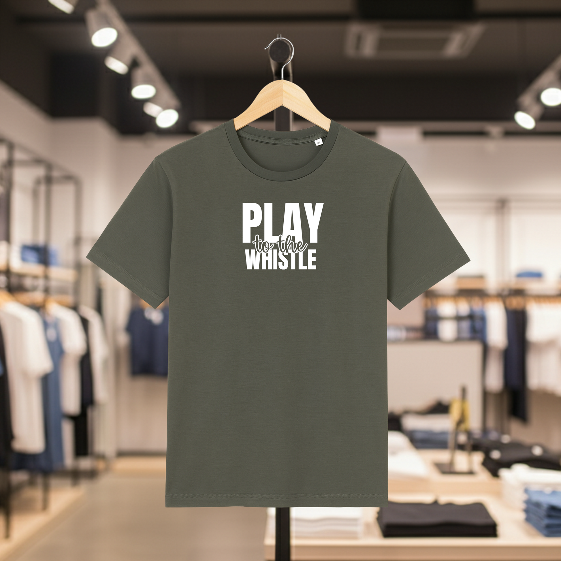 Khaki t-shirt with PLAY TO THE WHISTLE text on a hanger in a store setting