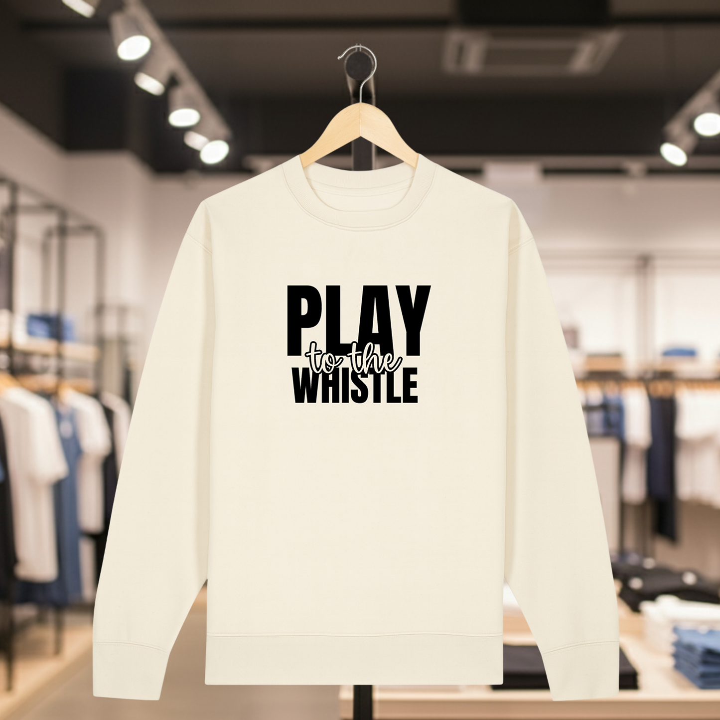 Natural sweatshirt with PLAY TO THE WHISTLE text on a hanger in a store setting