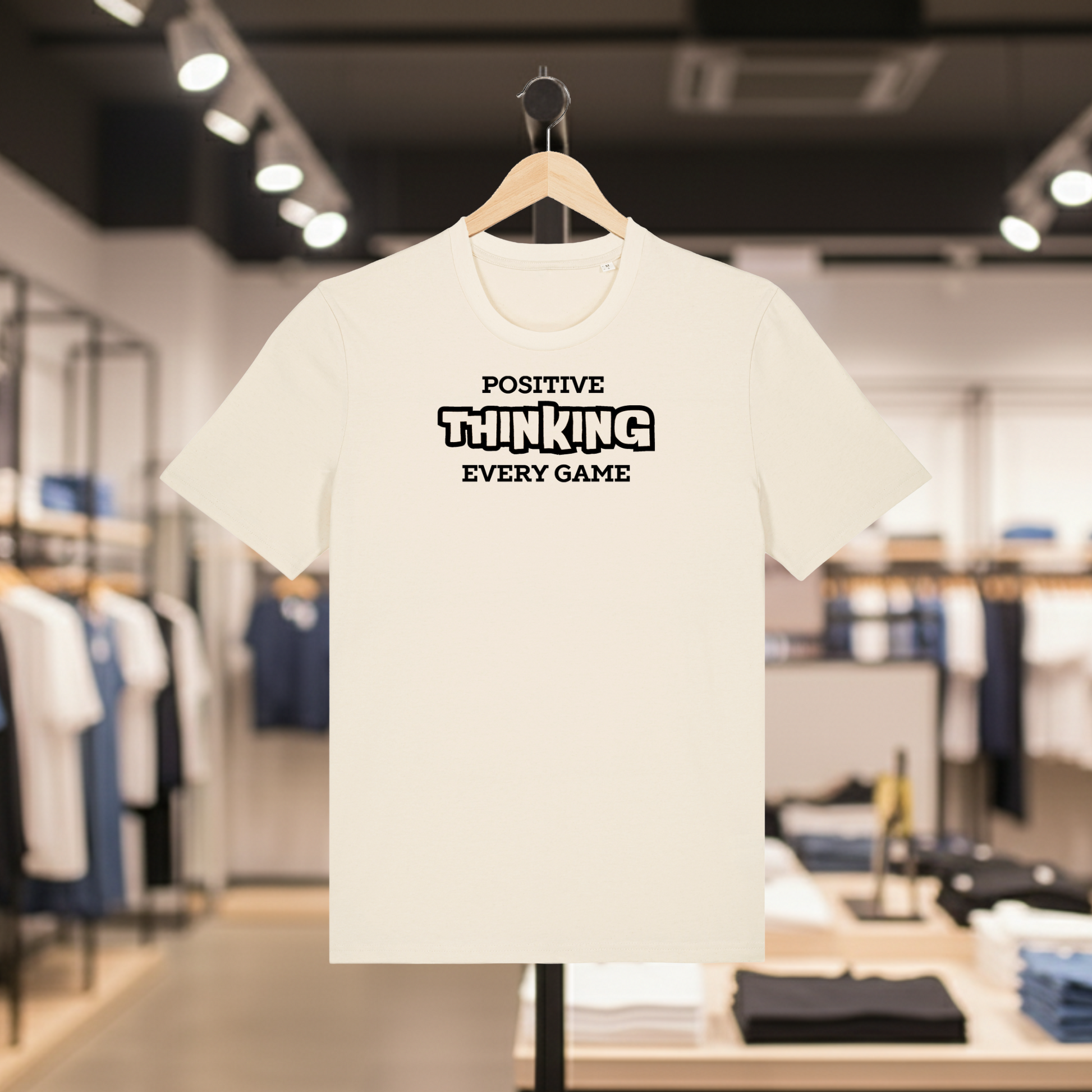 Natural t-shirt with POSITIVE THINKING EVERY GAME text on a hanger in a store setting.