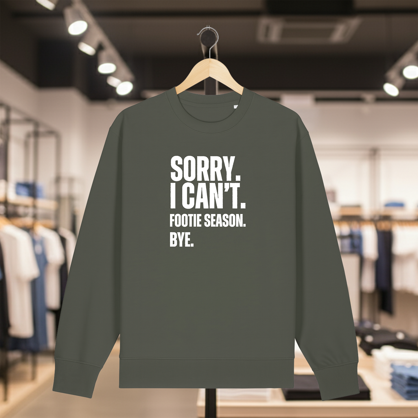 Khaki sweatshirt with white text SORRY. I CAN'T. FOOTIE SEASON. BYE. on a hanger in a store setting
