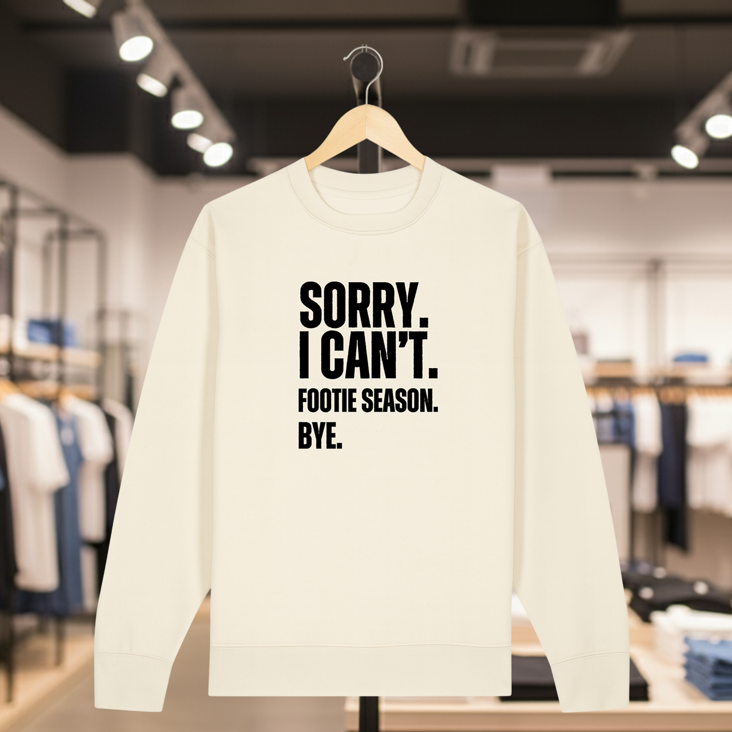 Natural sweatshirt with white text SORRY. I CAN'T. FOOTIE SEASON. BYE. on a hanger in a store setting