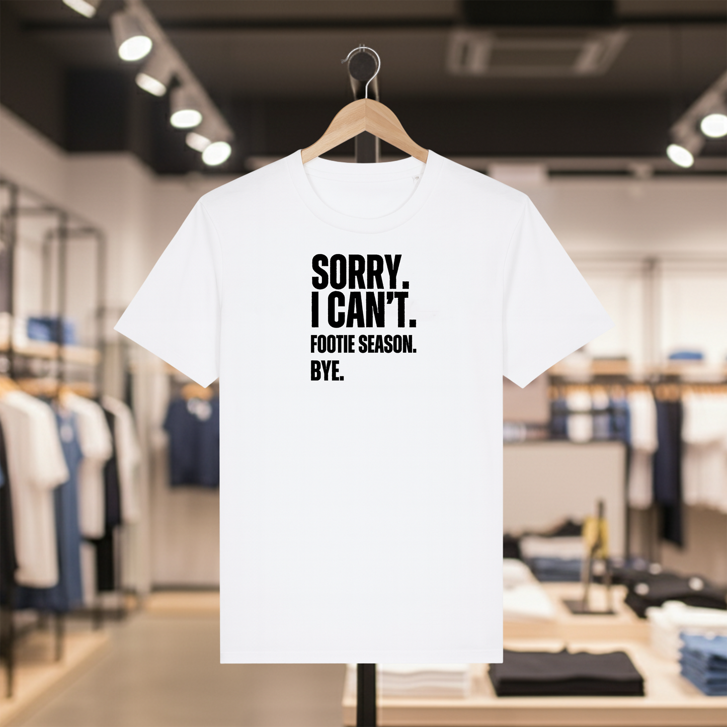 White t-shirt with SORRY. I CAN'T. FOOTIE SEASON. BYE. text on a hanger in a store setting.