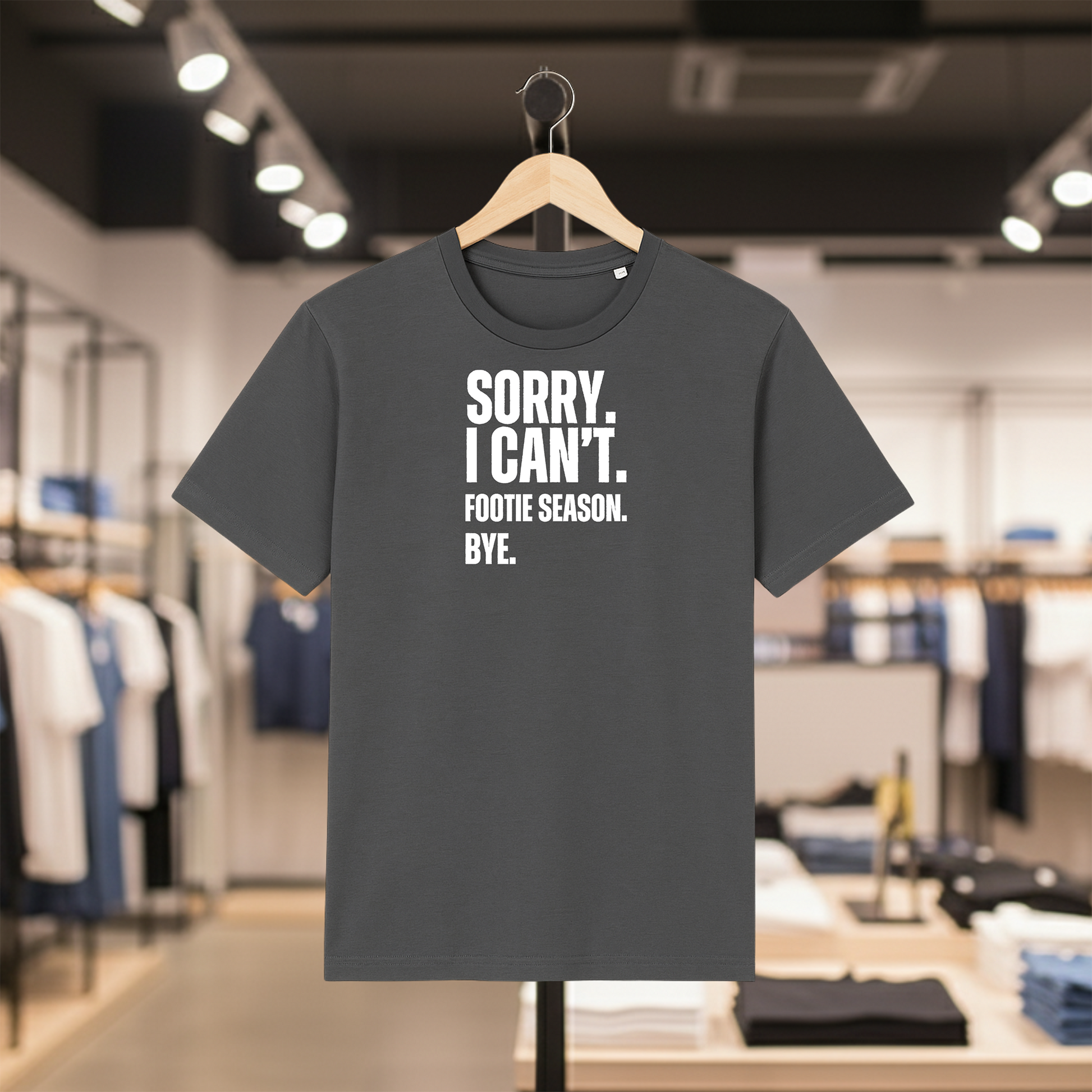 Grey t-shirt with SORRY. I CAN'T. FOOTIE SEASON. BYE. text on a hanger in a store setting.