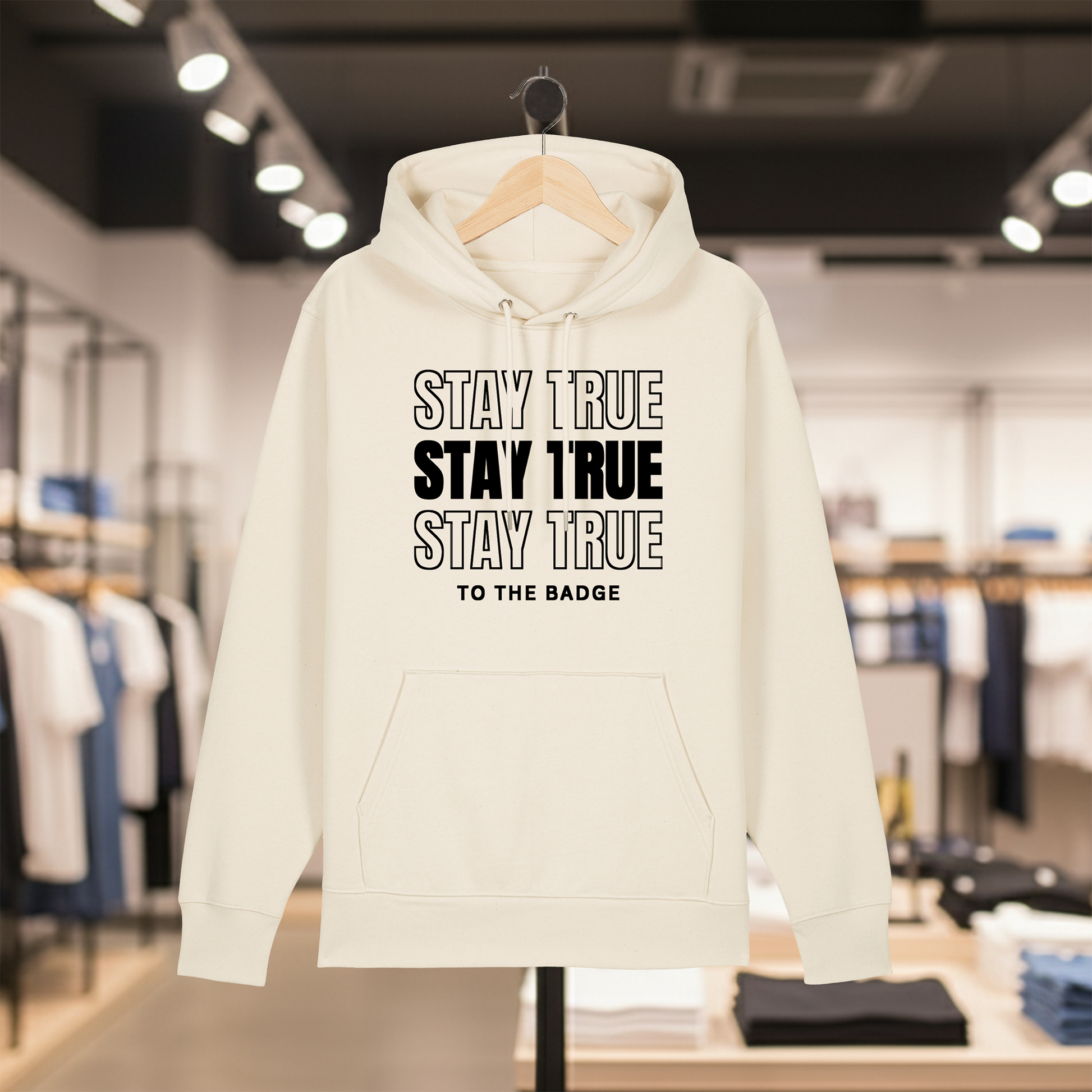 Natural hoodie with text STAY TRUE TO THE BADGE on a hanger in a store setting
