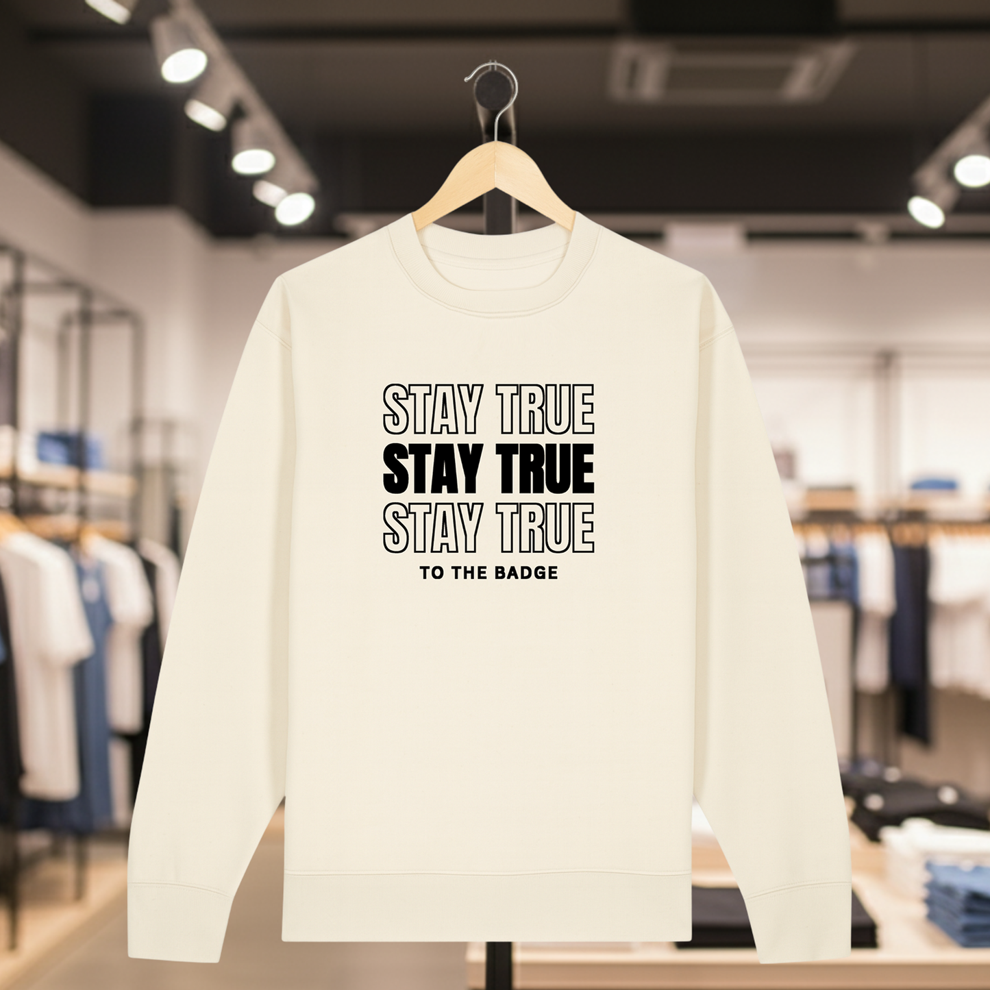 Natural sweatshirt with text STAY TRUE TO THE BADGE on a hanger in a store setting