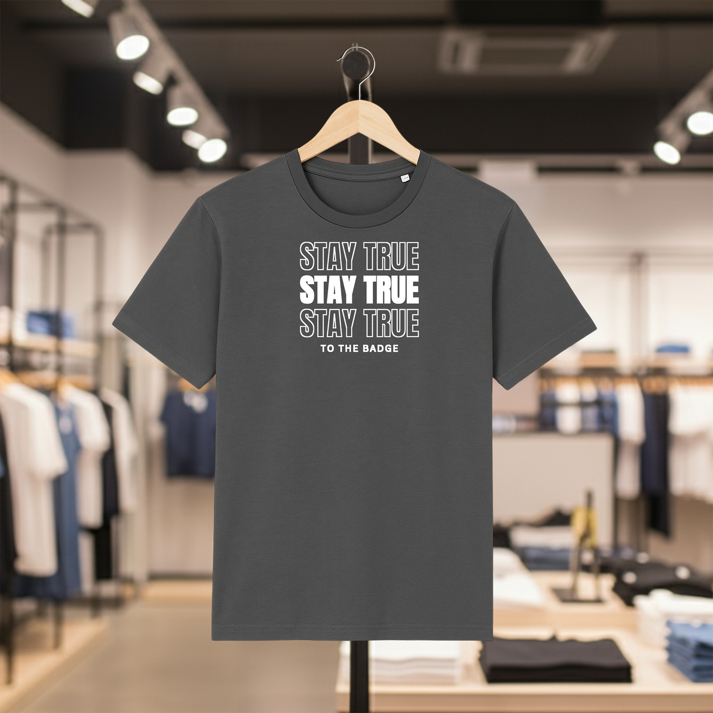 Grey t-shirt with STAY TRUE TO THE BADGE text on a hanger in a store setting