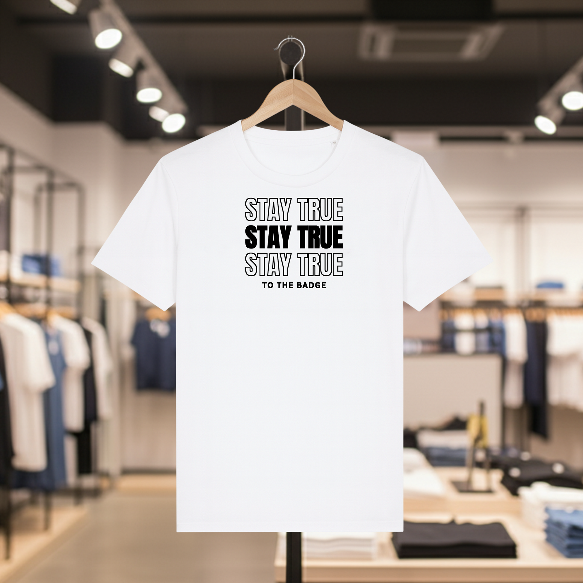 White t-shirt with STAY TRUE TO THE BADGE text on a hanger in a store setting