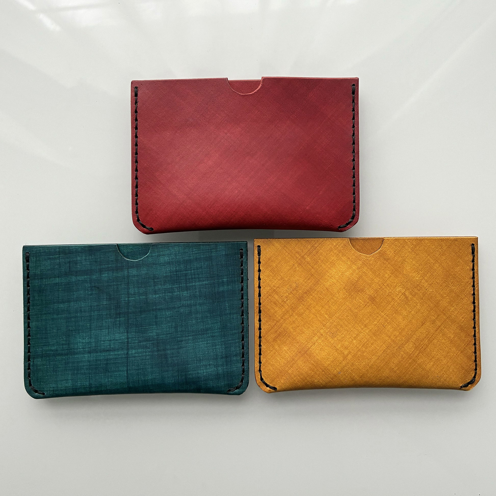 Three leather card wallets in colours yellow, teal and red on a white background