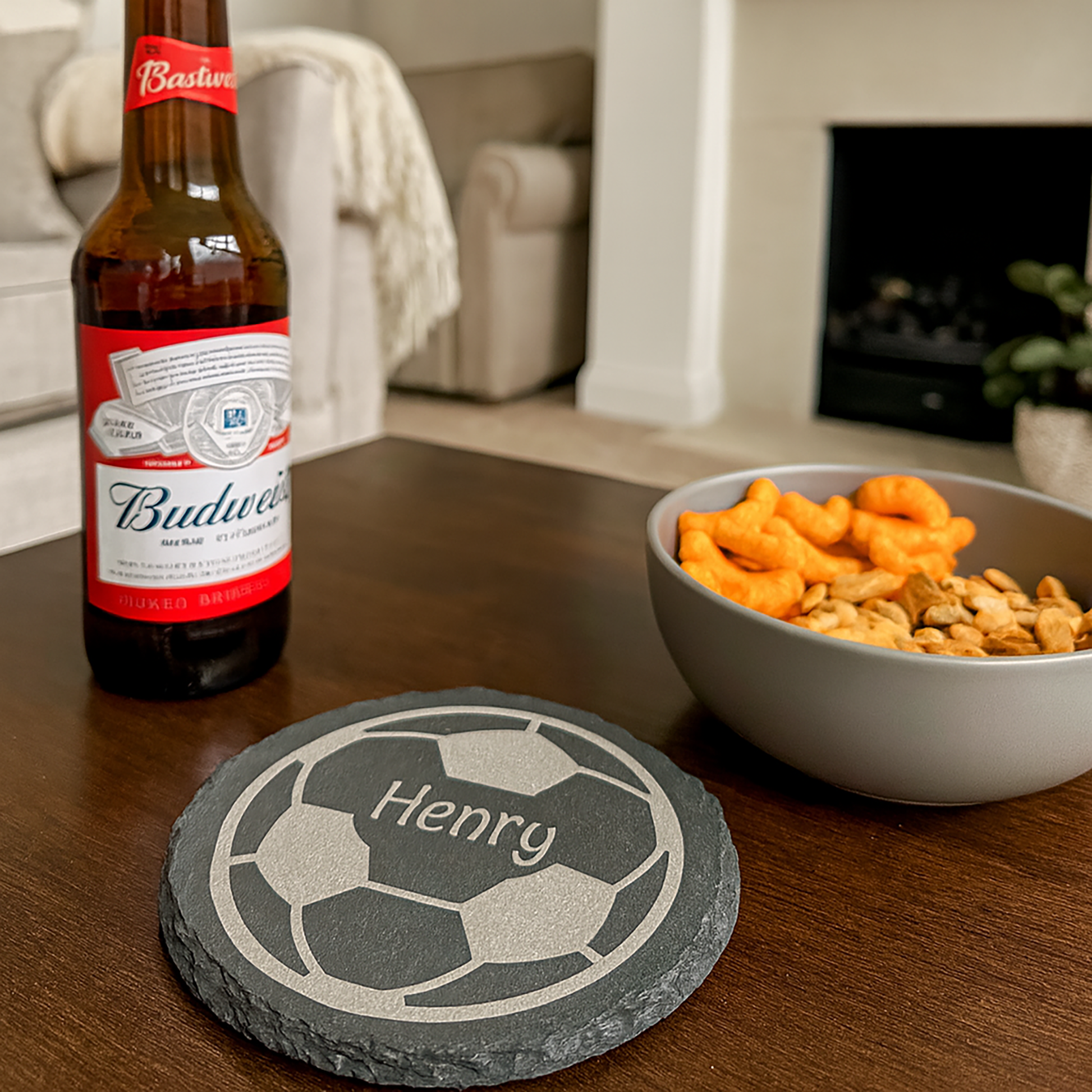 A slate coaster engraved with a football and the name 'Henry' on a table with snacks.